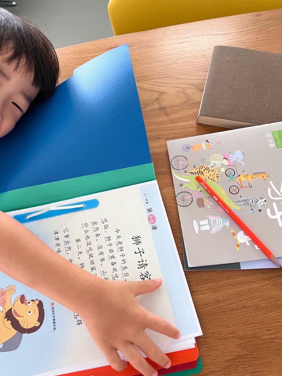 A child resting his head on the table next to his Chinese homework